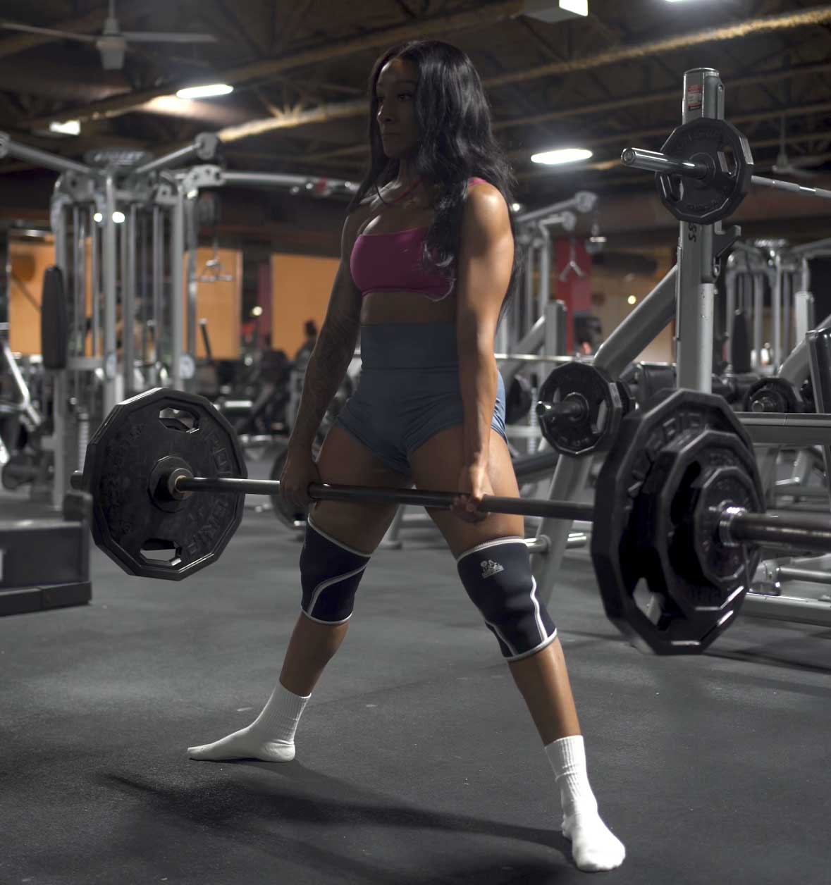 Coach standing upright in a gym, holding a weight.